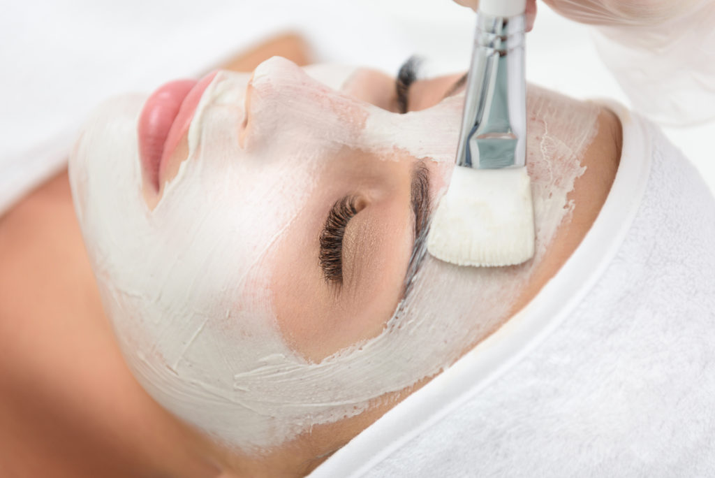 Close up of woman face enjoying healthy procedure at spa. Beautician is applying clay on her skin | RefineKC Aesthetics in Kansas City, MO